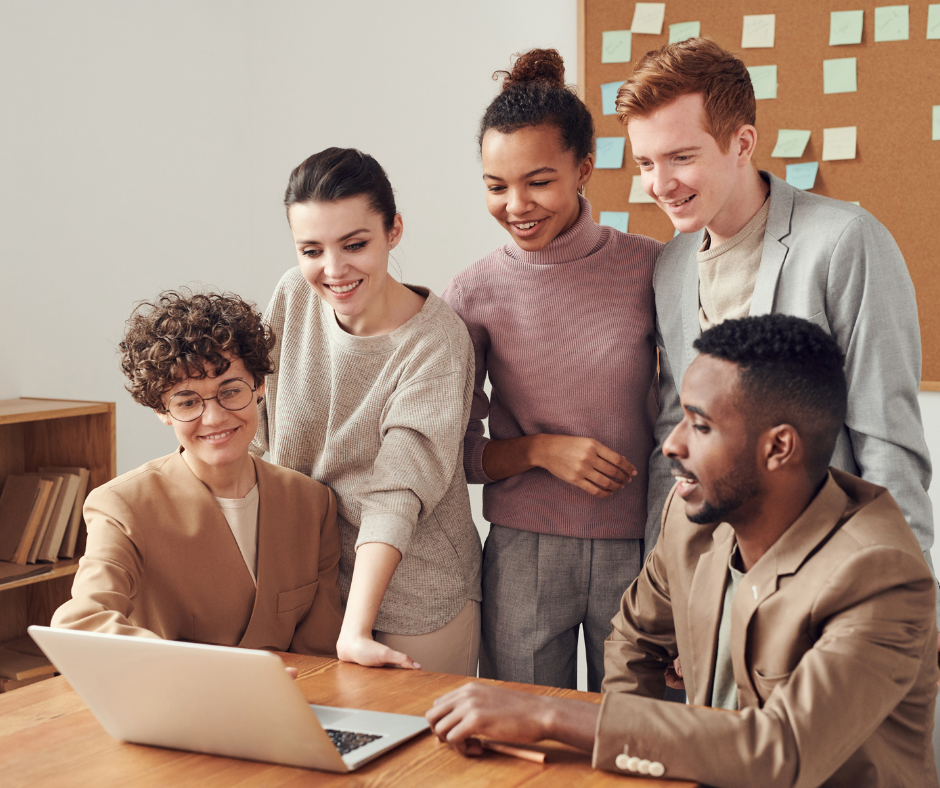 group of young adults smiling around a laptop