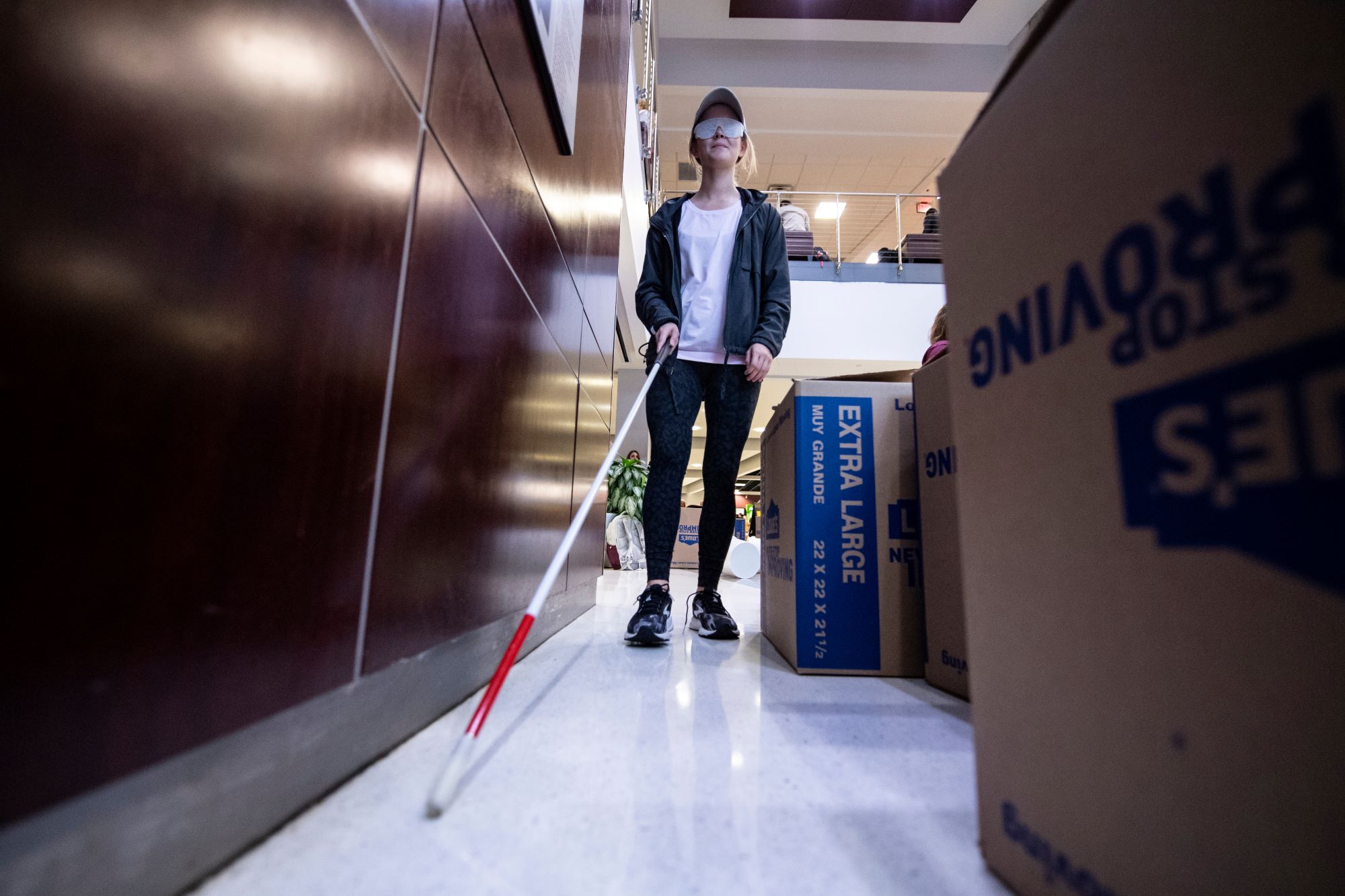 College student using a white cane to navigate around boxes