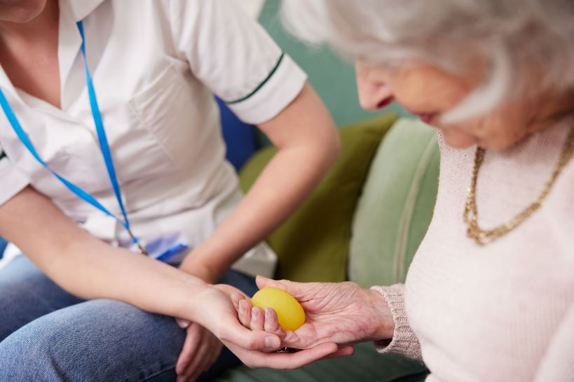 An occupational therapist helping an older woman squeeze a therapy ball.