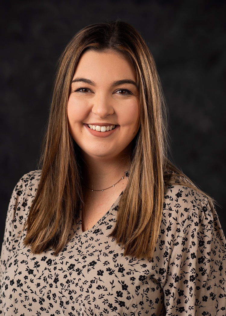 Headshot of Lindsey Speights. Lindsey has brown hair and is wearing a beige shirt decorated with small black flowers.