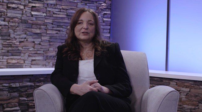 Video presenter Sylvia is sitting on an armchair with her hands in her lap in a brightly lit studio.