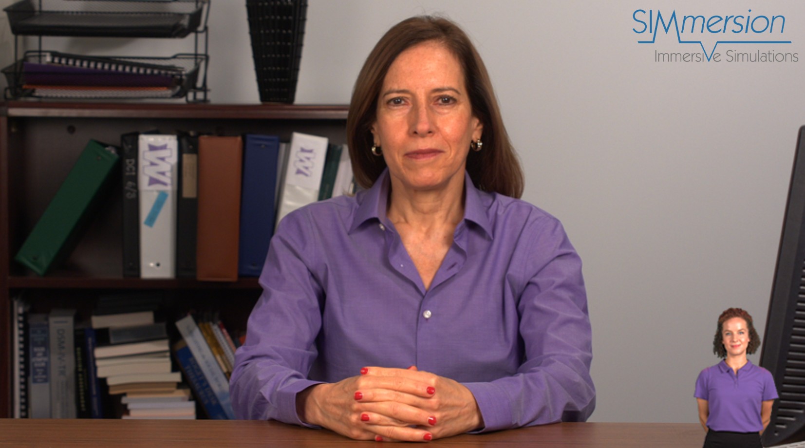 Simulation of a job coach sitting at a desk. She is middle-aged with brown hair and is wearing a purple blouse.