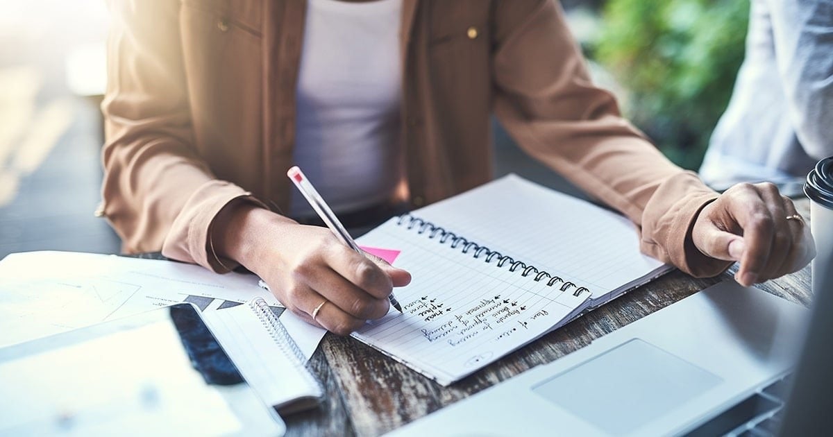 Woman sitting on a desk writing in a notebook.
