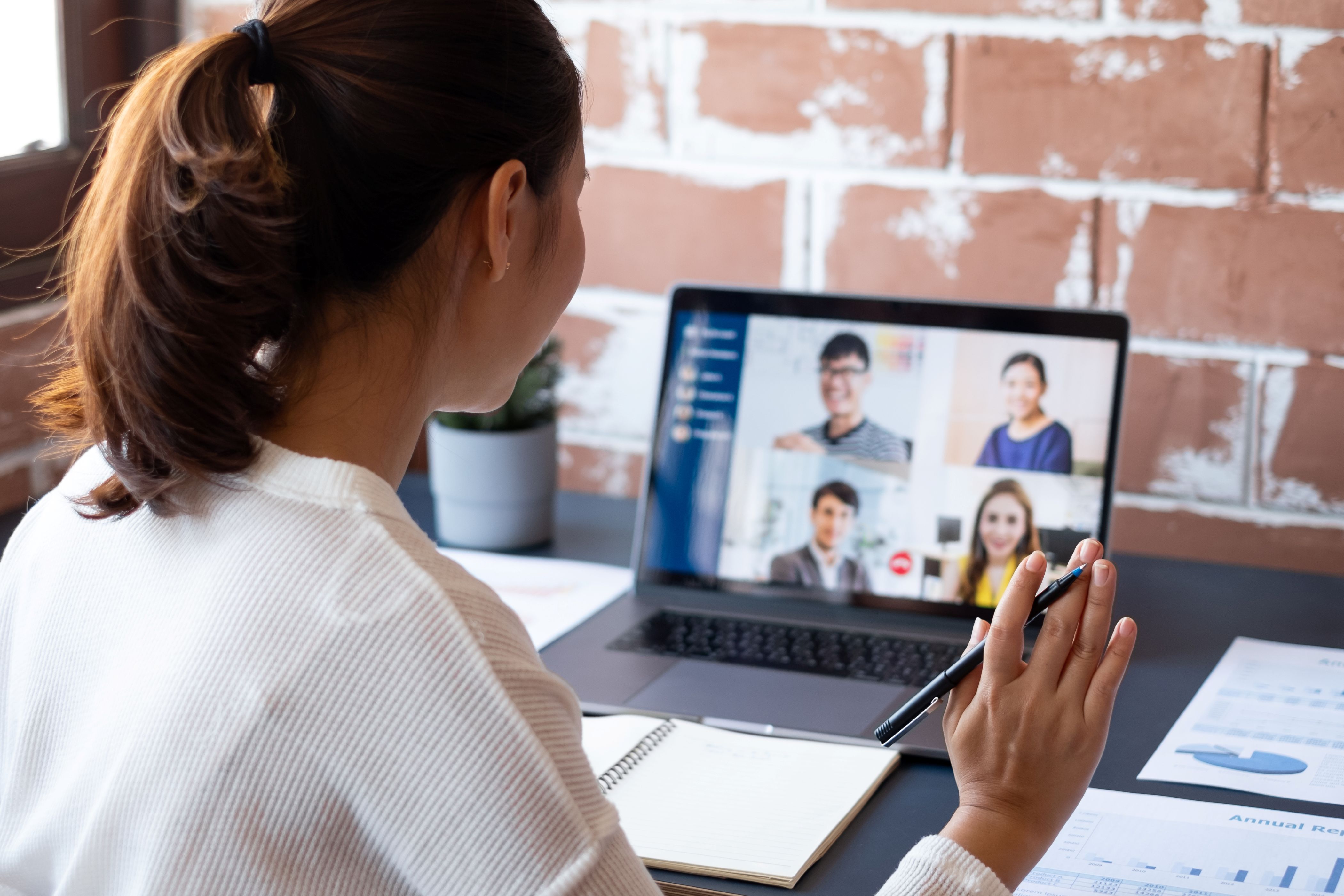 Woman sitting at a desk waving at screen during a virtual meeting.