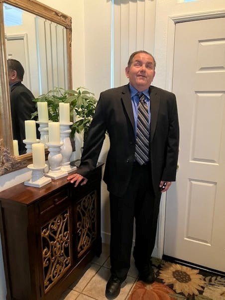 Headshot of Richard Rueda. He is wearing a suit and tie and is standing in a house.
