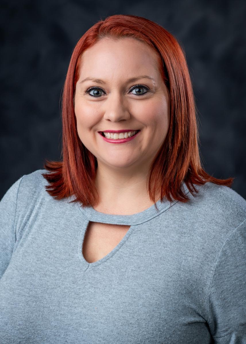 Headshot of Brittany Greer. Brittany has red hair and is wearing a teal blouse.