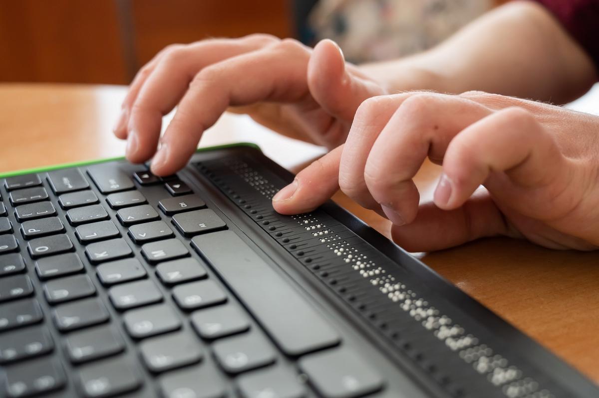 Close up of a pair of hands using a braille keyboard.