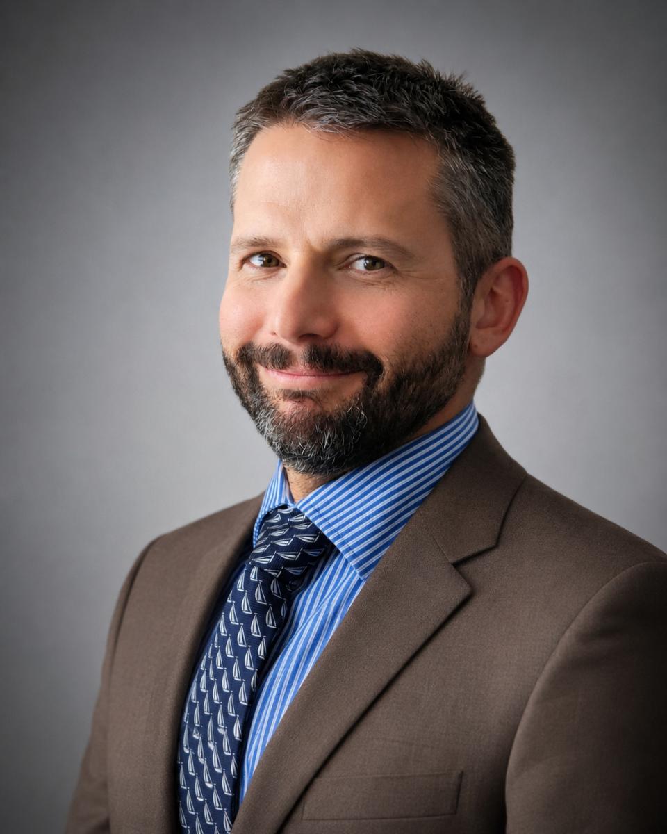 Headshot of TJ. He is wearing a grey business suit and is smiling.